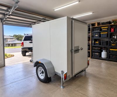 Low profile coolroom trailer parked inside a garage with the roller door up, showing it fits under a standard domestic door